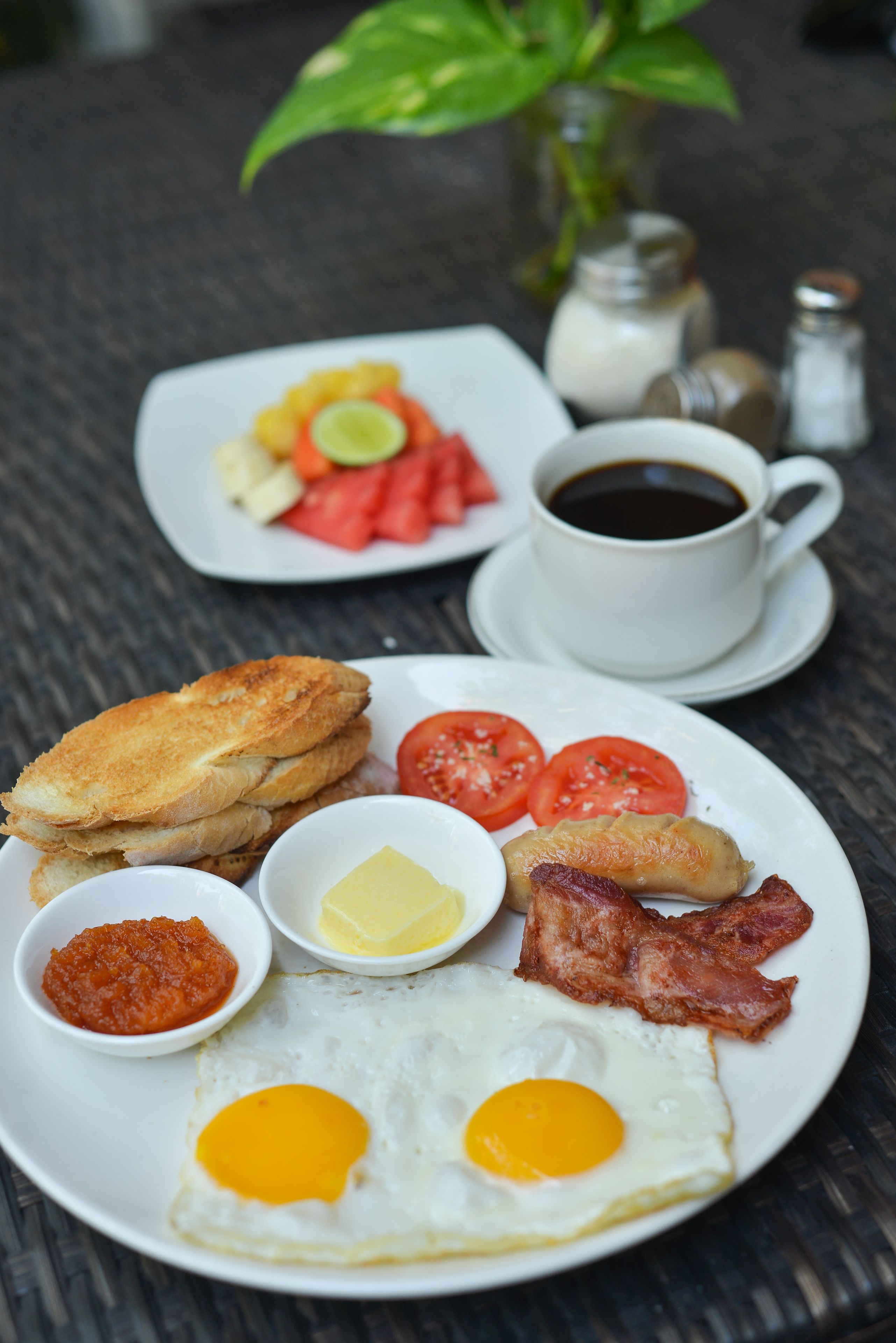 A breakfast plate with eggs, bacon, tomatoes, toast, and a cup of coffee.