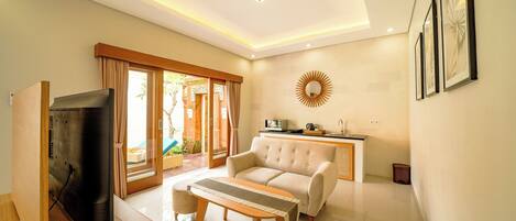 A modern living room with a sofa, a coffee table, a TV, and a dining area with a kitchen counter.