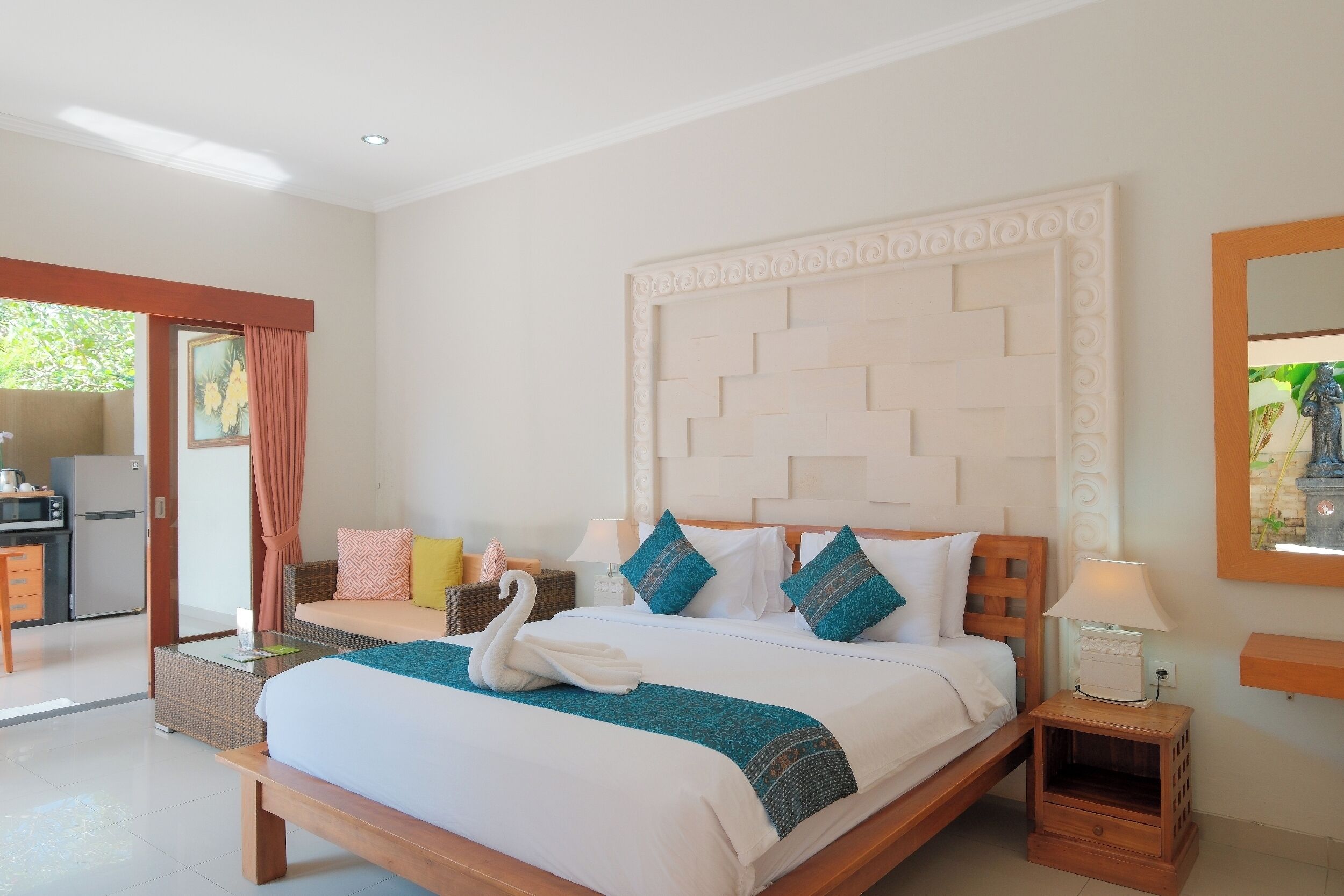 A hotel room with a bed, a bedside table, a lamp, a wall-mounted mirror, and a view of the outside.