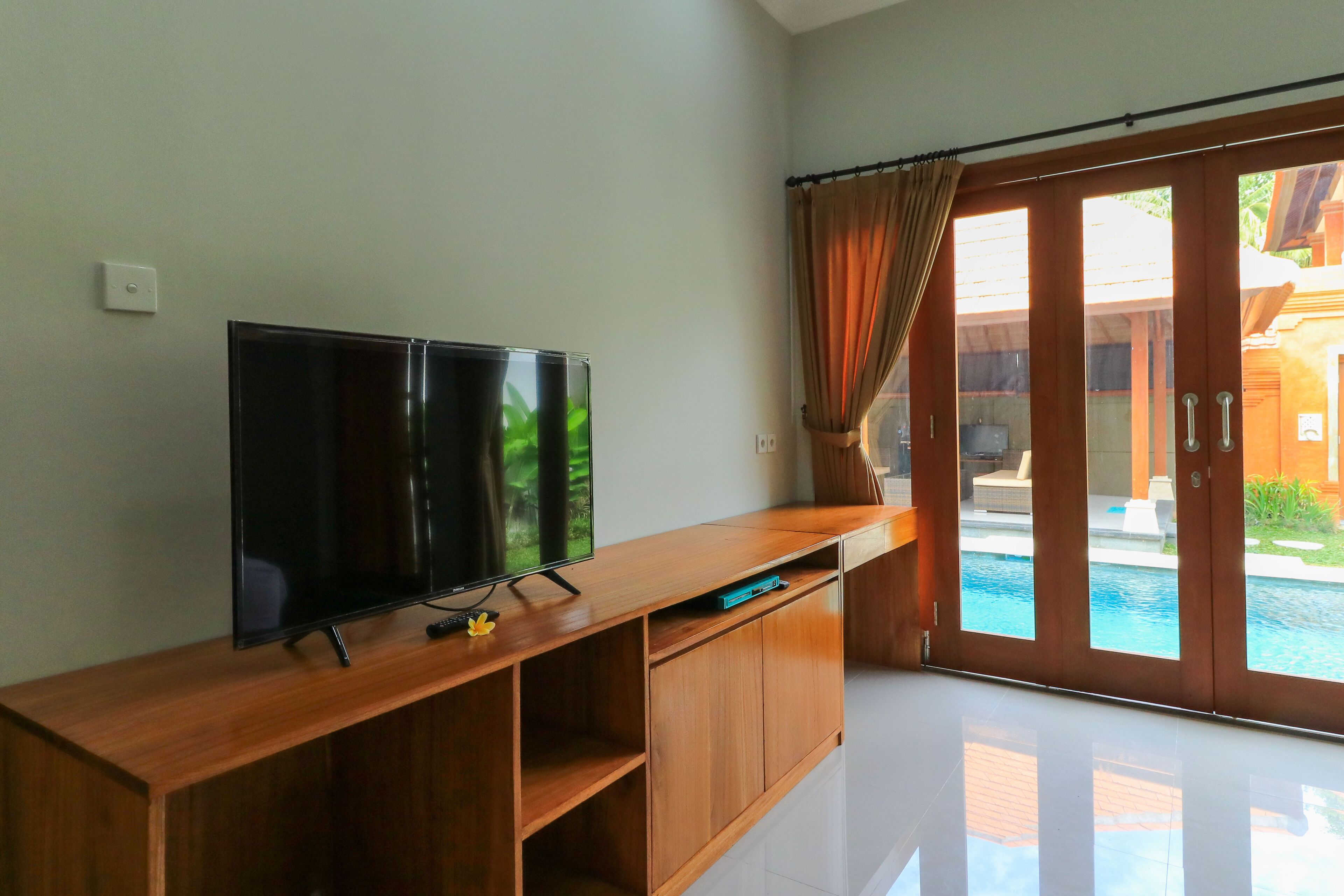 A room with a wooden TV stand, a flat-screen TV, and a sliding glass door leading to a pool area.