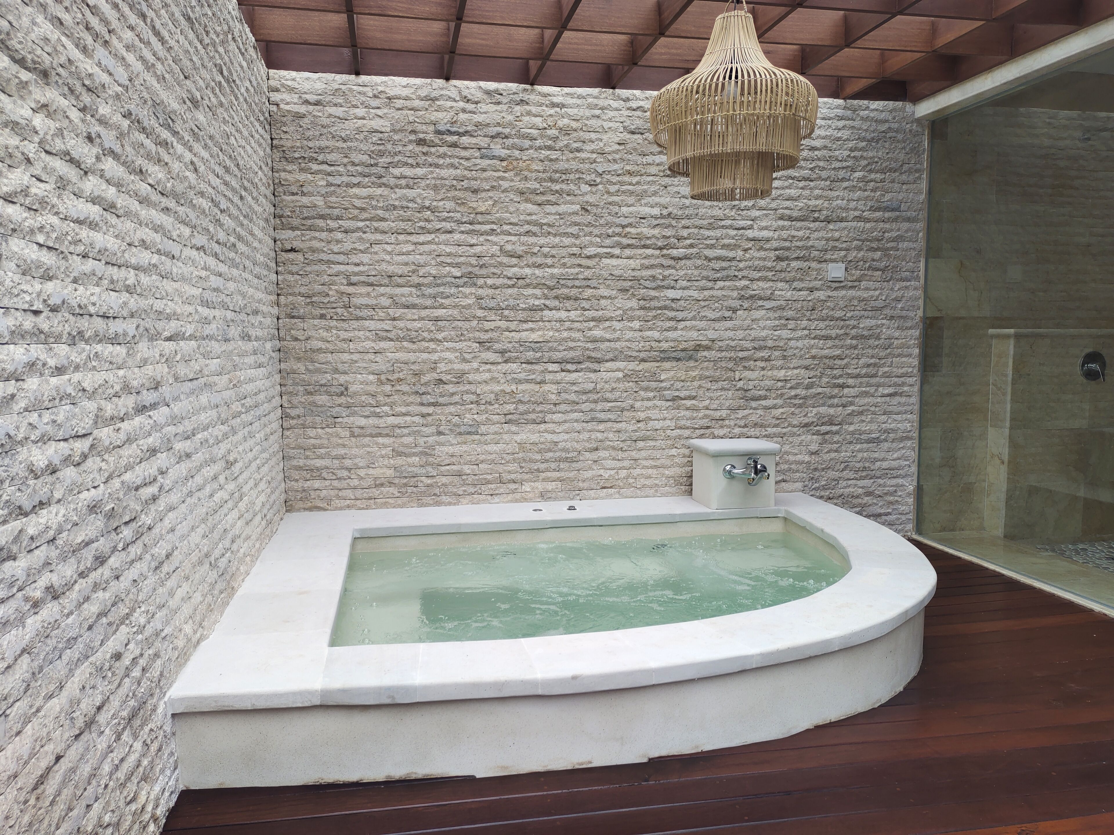 A modern bathroom with a stone wall, a freestanding bathtub, and a glass-enclosed shower area.