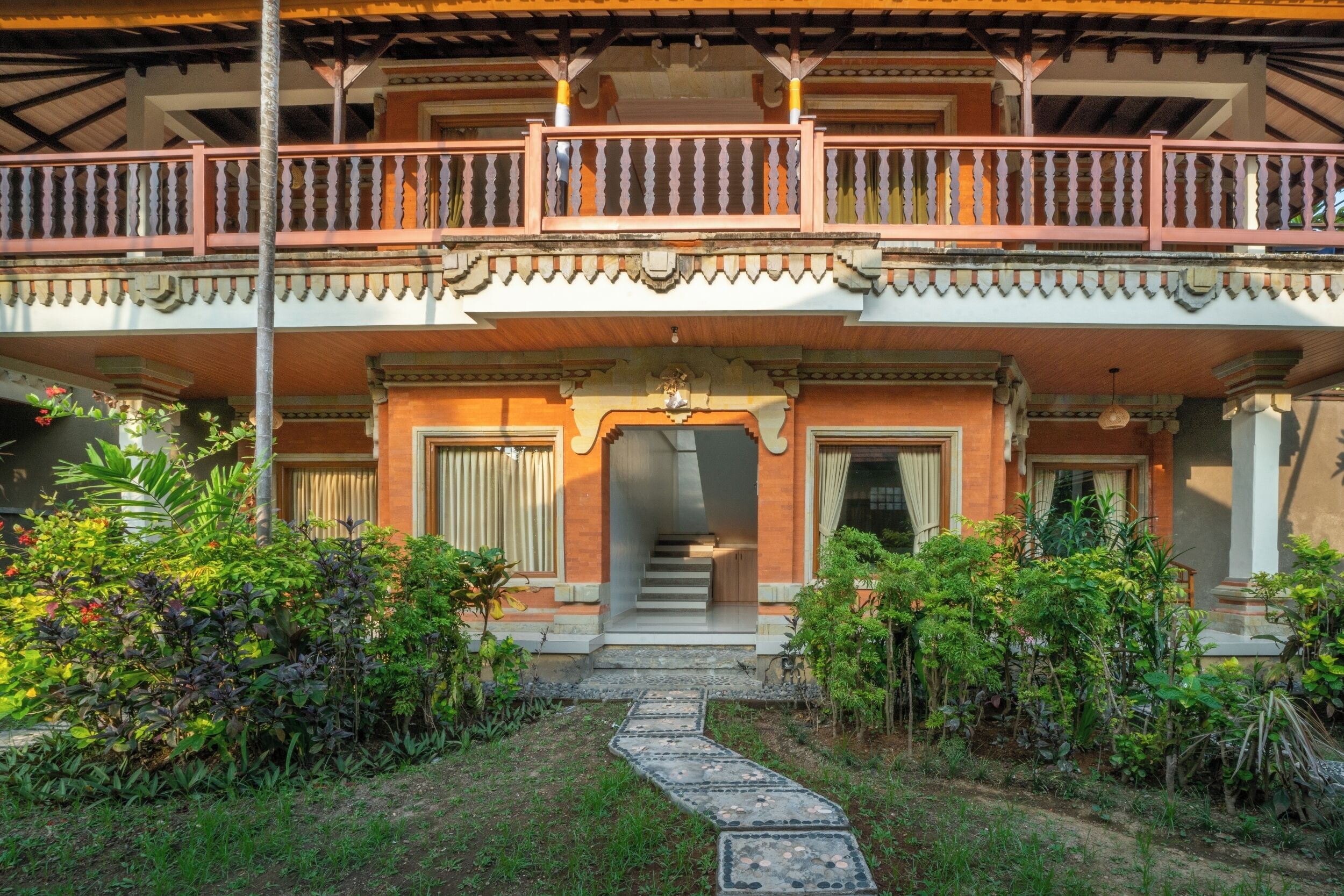 A traditional building with a balcony, a staircase leading to the entrance, and a garden pathway.