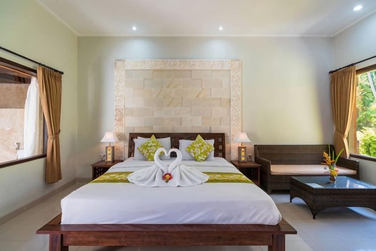 A hotel room with a large bed, two bedside tables with lamps, a sofa, and a decorative wall.