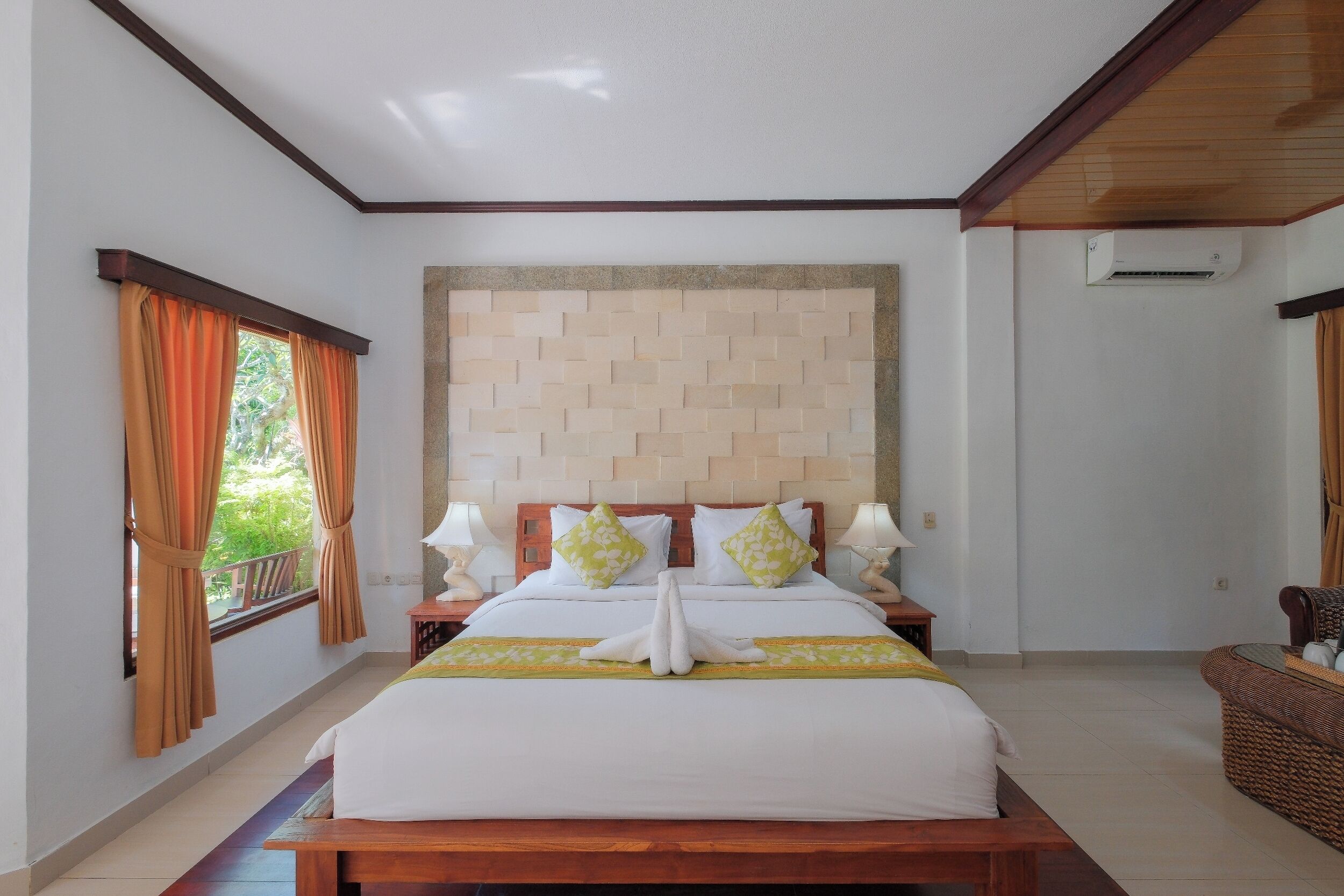 A hotel room with a bed, curtains, a headboard, bedside lamps, and a view of greenery.