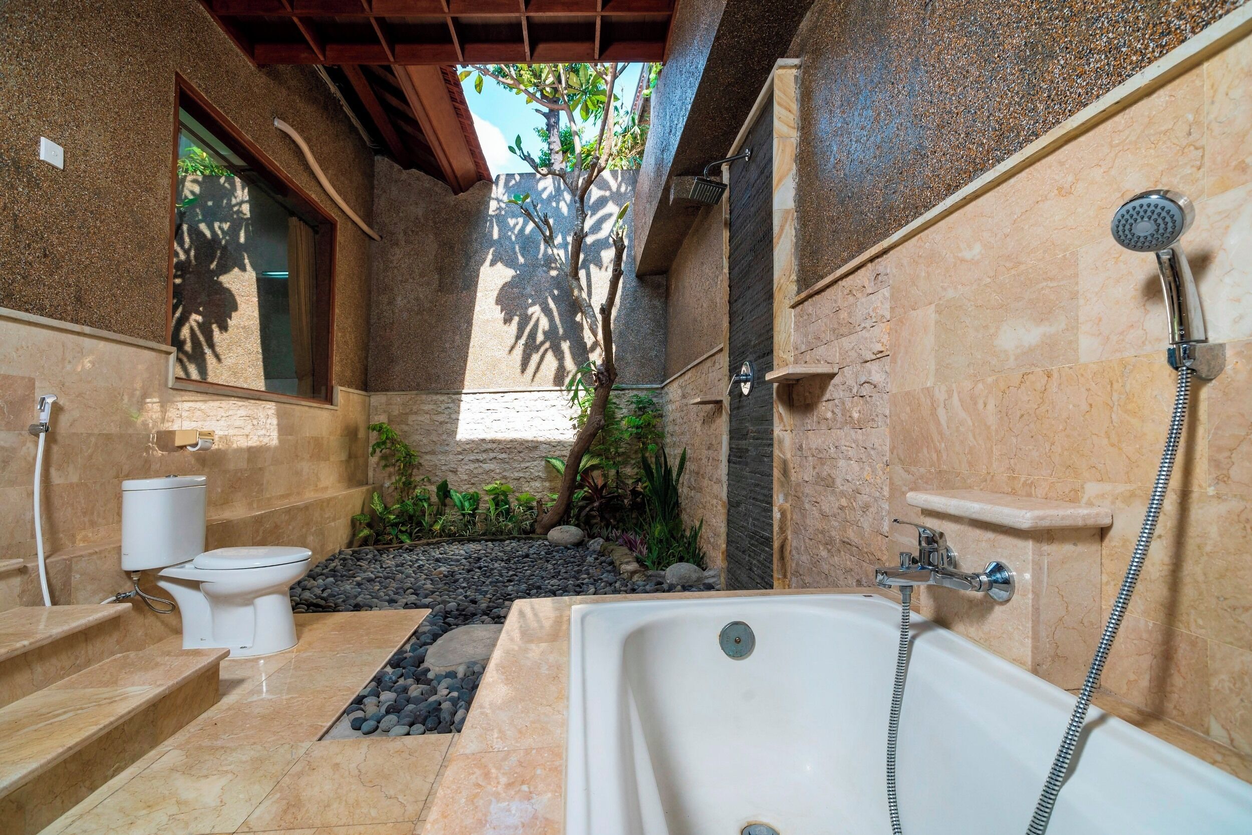 A bathroom with a bathtub, toilet, and sink, featuring stone walls and a small garden area.