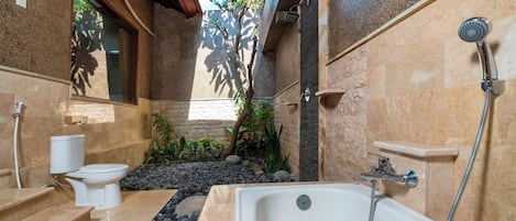 A bathroom with a bathtub, toilet, and sink, featuring stone walls and a small garden area.