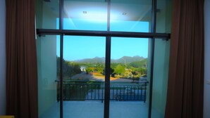 A room with a large sliding glass door leading to a balcony with a view of mountains and greenery. - Takhun Mountain View Hotel (Ban Ta Khun)