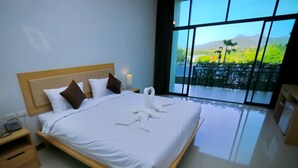 A modern hotel room with a large bed, wooden headboard, white linens, and a view of a lush landscape through large windows. - Takhun Mountain View Hotel (Ban Ta Khun)