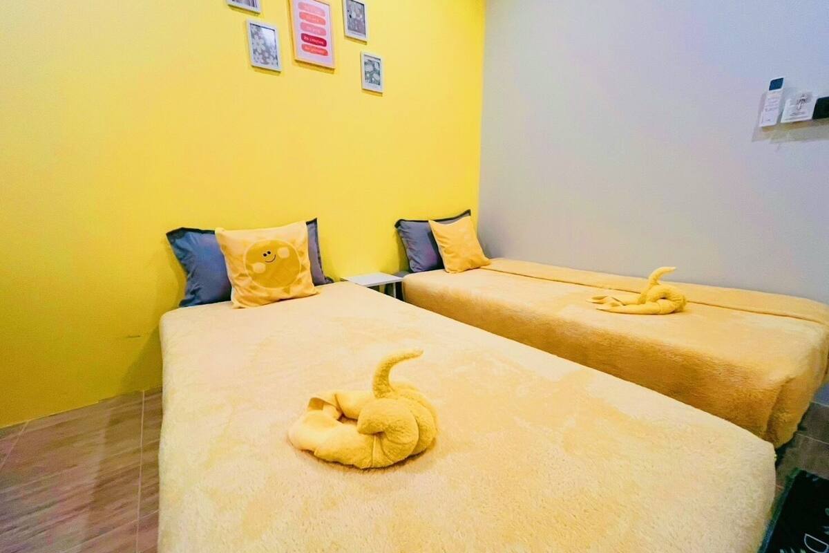 A room with two beds, each with a yellow blanket and a decorative swan pillow.