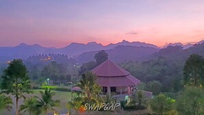A traditional building with a red roof, surrounded by lush greenery and mountains in the background. - Takhun Mountain View Hotel (Ban Ta Khun)