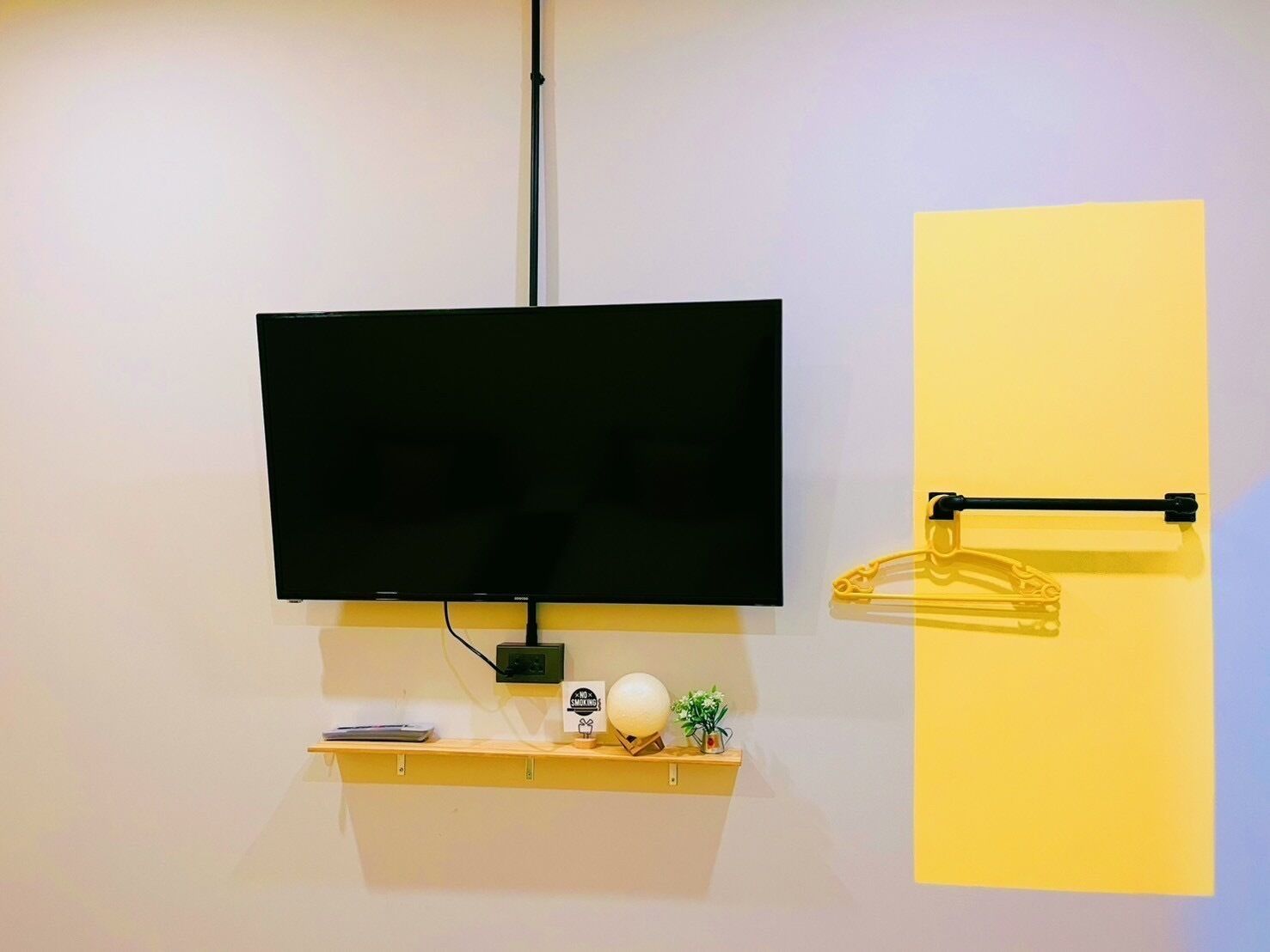 Una TV a schermo piatto montata a parete, un piccolo ripiano con alcuni oggetti e una porta con maniglia nera.