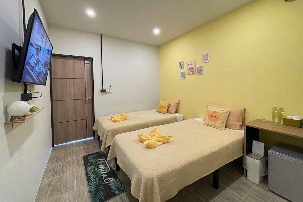 A hotel room with two beds, a TV, a desk, and a trash bin.
