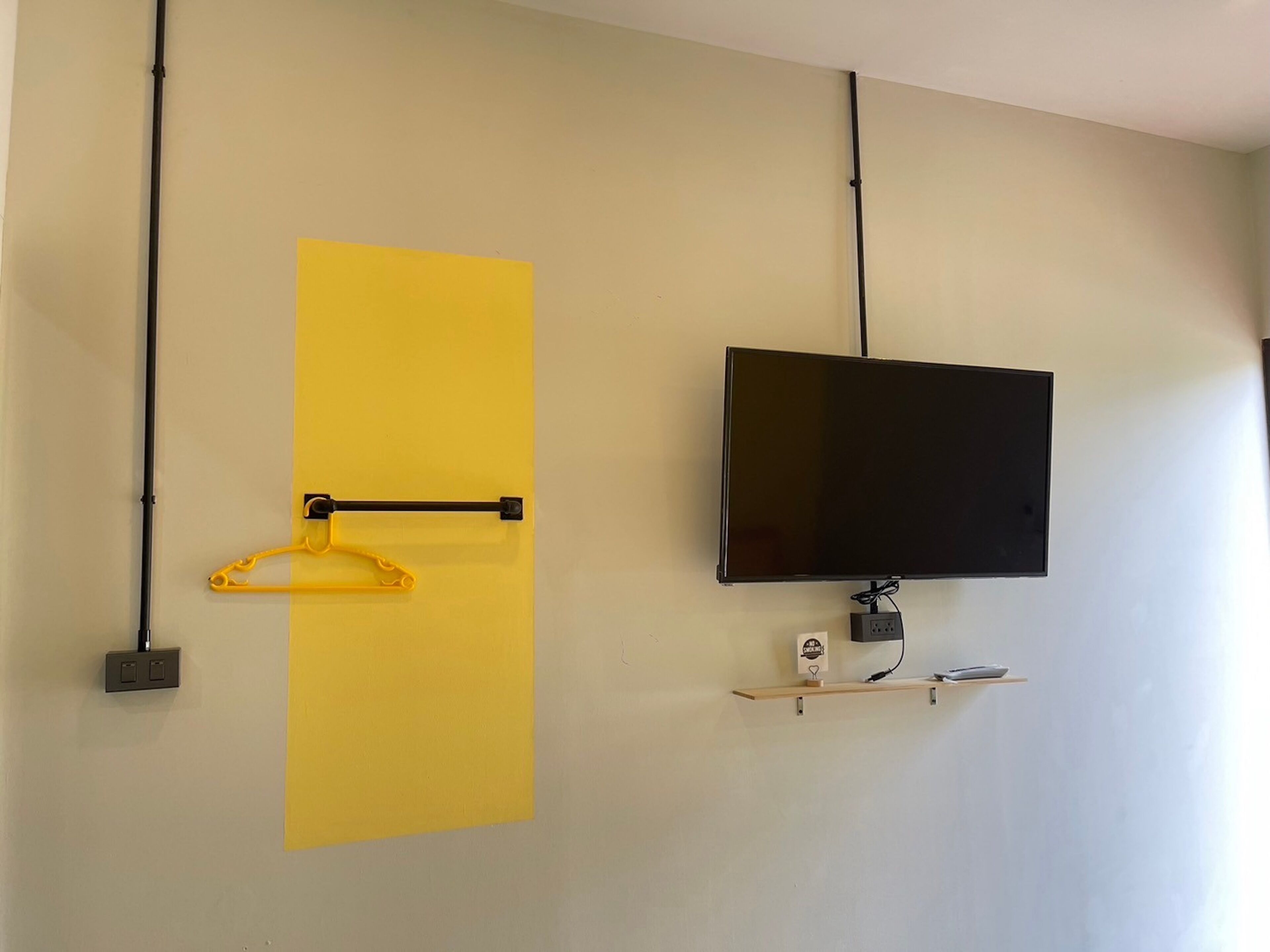 Ein Zimmer mit einem an der Wand befestigten Flachbildfernseher, einem gelben, vertikalen Streifen an der Wand und einem hängenden, gelben Gegenstand.