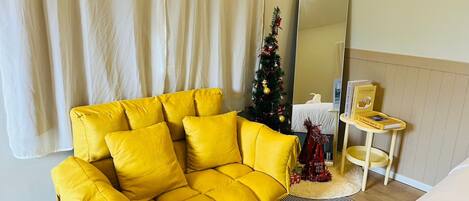 A yellow sofa in a room with a Christmas tree, a mirror, and a small table with a book.