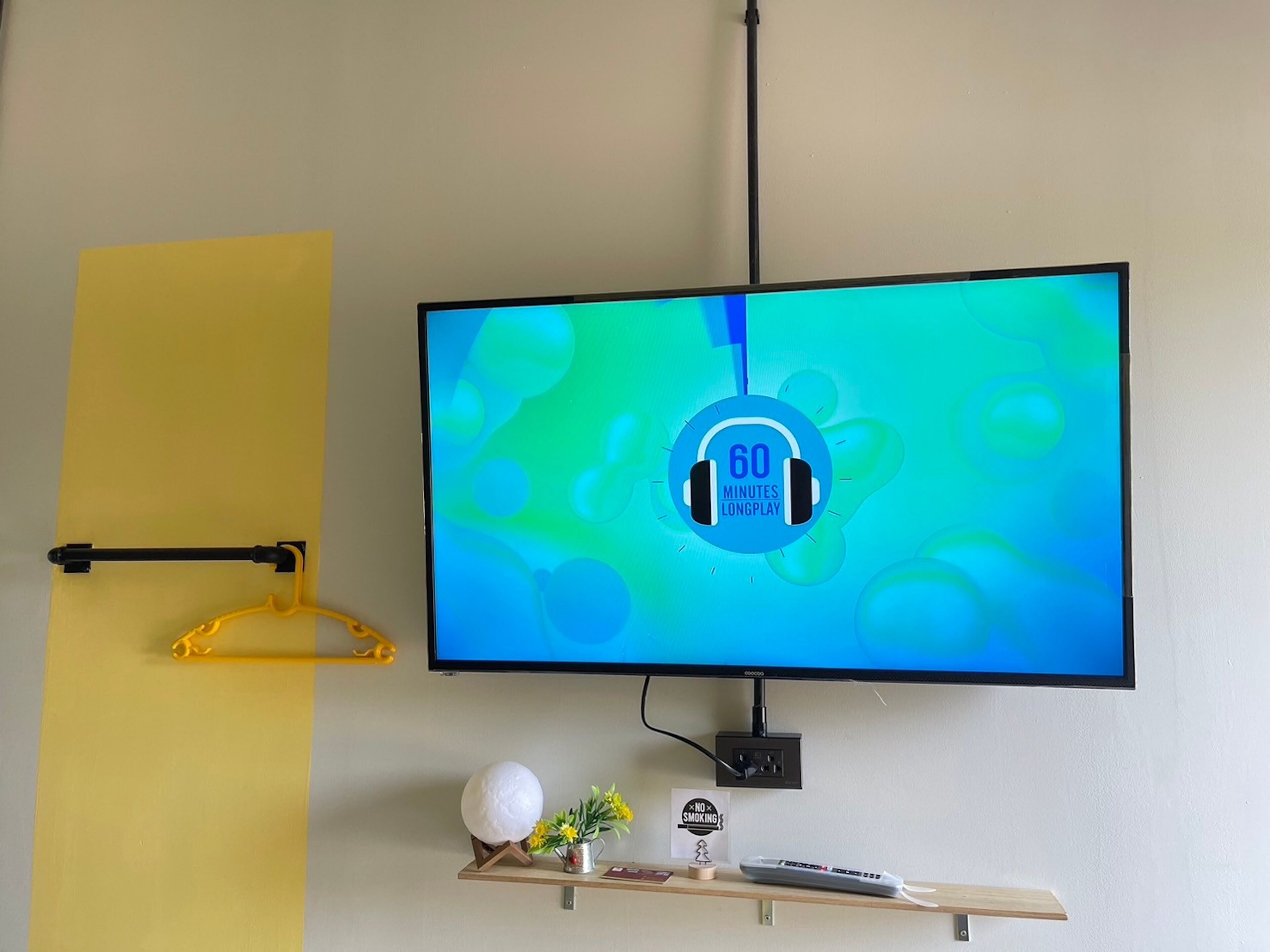 A television mounted on a wall with a blue screen displaying a timer icon. Below the TV, there is a shelf with a remote control, a decorative globe, and a small plant.