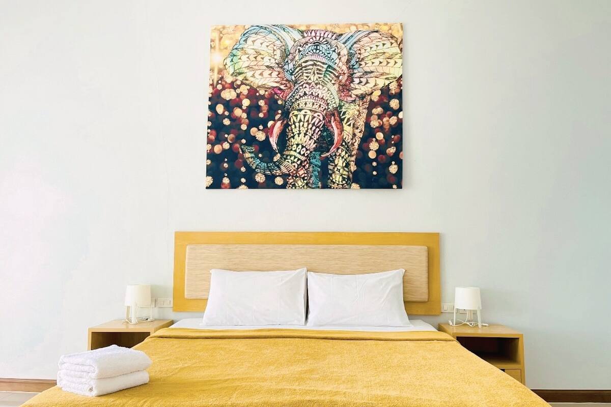 A hotel room with a bed, two bedside tables, and a wall-mounted artwork of an elephant.