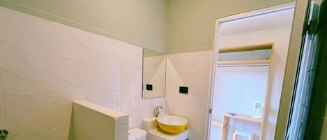 Un baño pequeño con un lavamanos blanco, un espejo y un taburete.