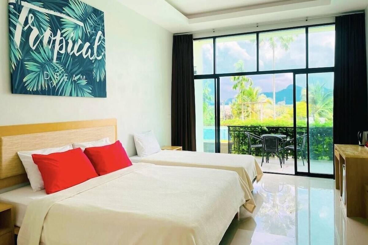 A hotel room with two beds, a large window with a view of greenery and mountains, and a tropical-themed wall art.