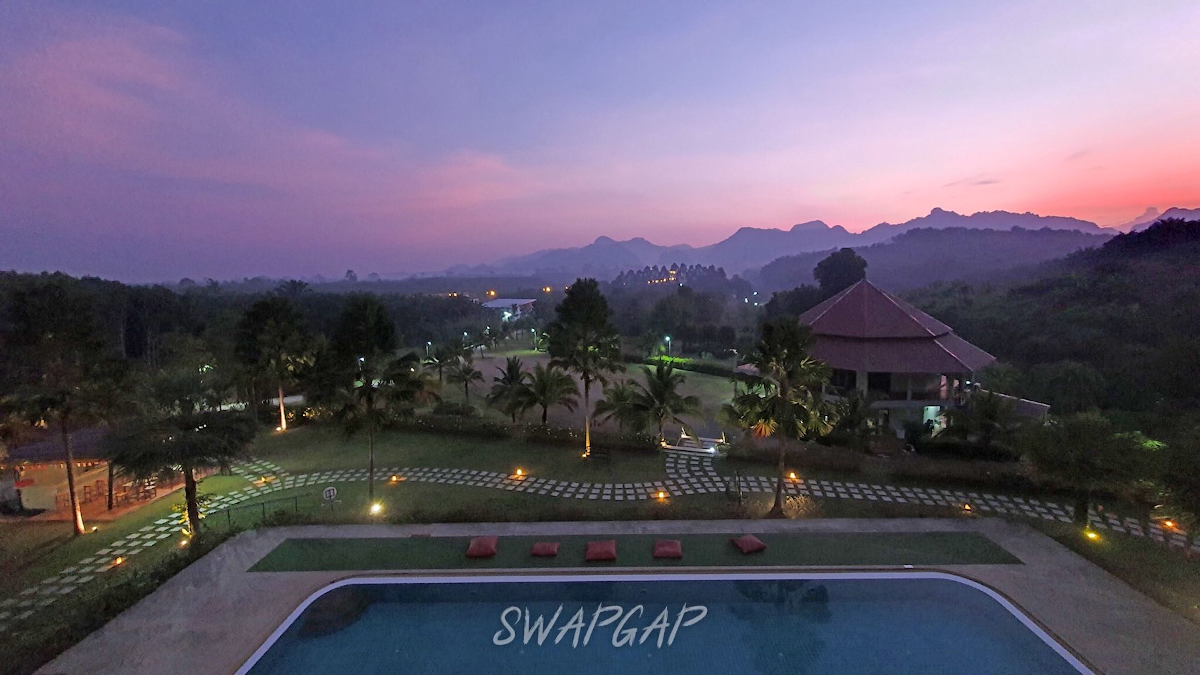A resort with a pool labeled 'SWAP GAP', surrounded by landscaped gardens, palm trees, and a view of distant mountains.