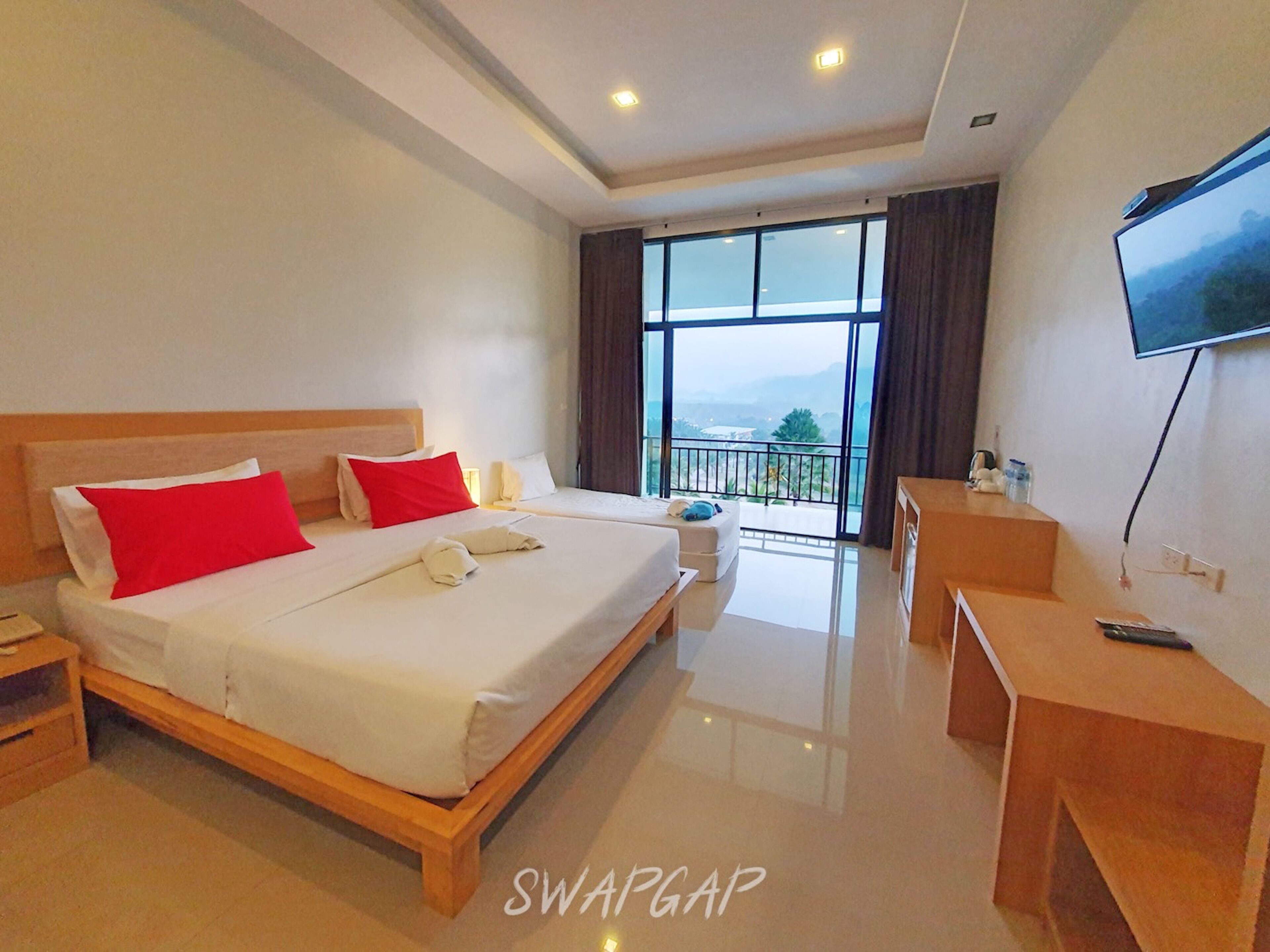 A hotel room with a large bed, a desk, a TV, and a balcony with a view.