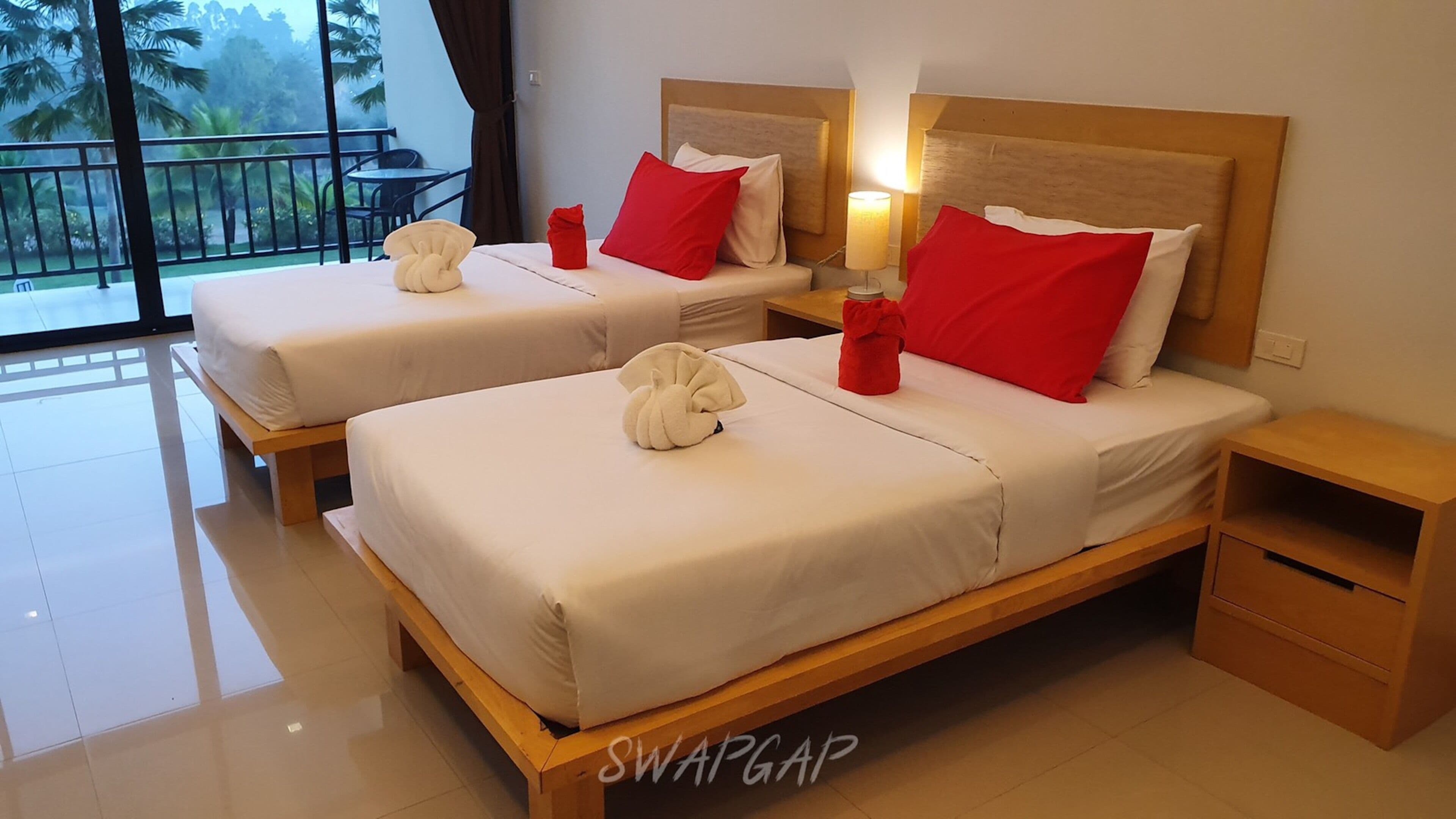 A hotel room with two beds, each with white linens and red pillows, a wooden headboard, and a nightstand.