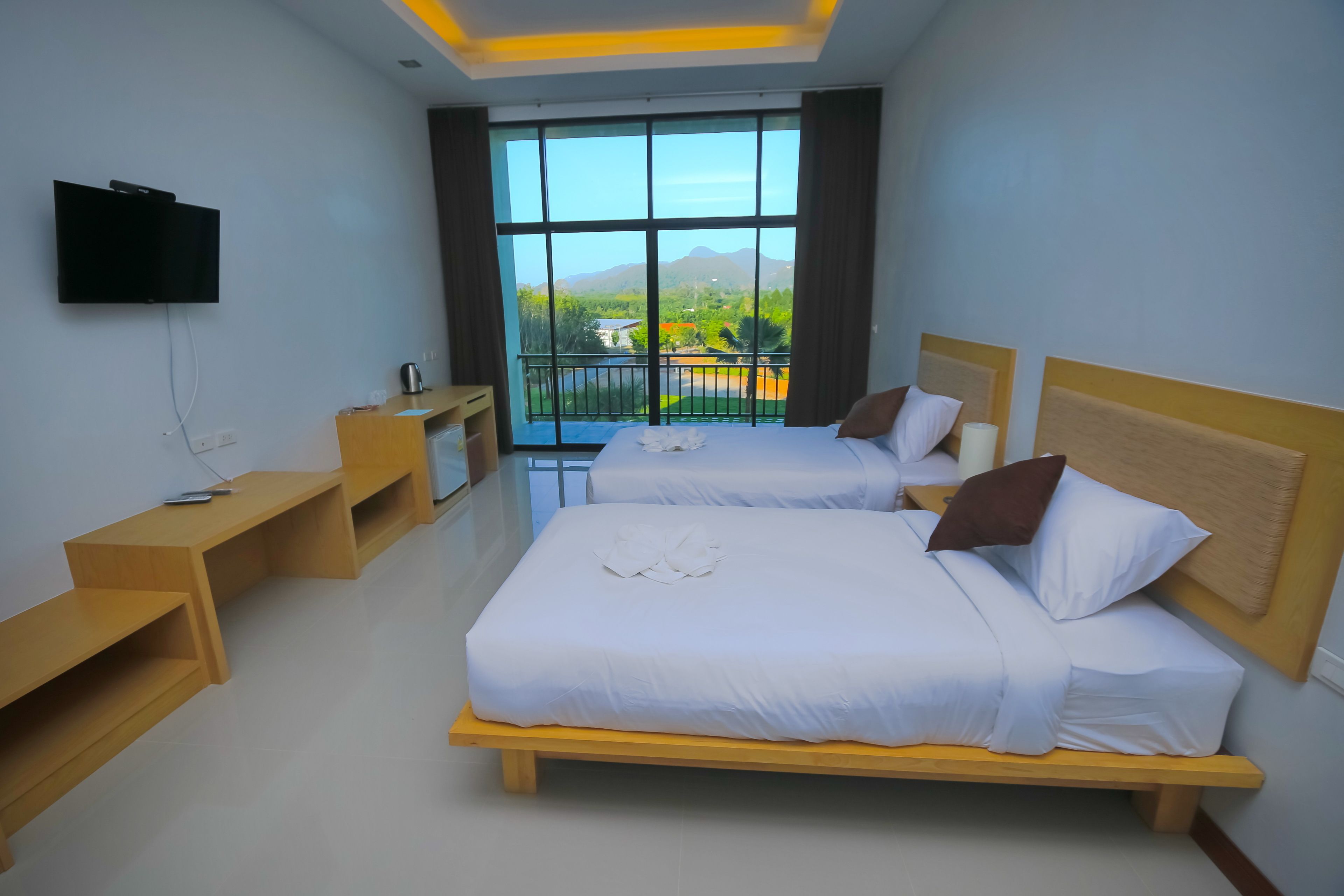 A hotel room with two beds, a TV, a wooden nightstand, and a large window with a view of mountains.
