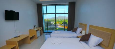 A hotel room with two beds, a TV, a wooden nightstand, and a large window with a view of mountains.