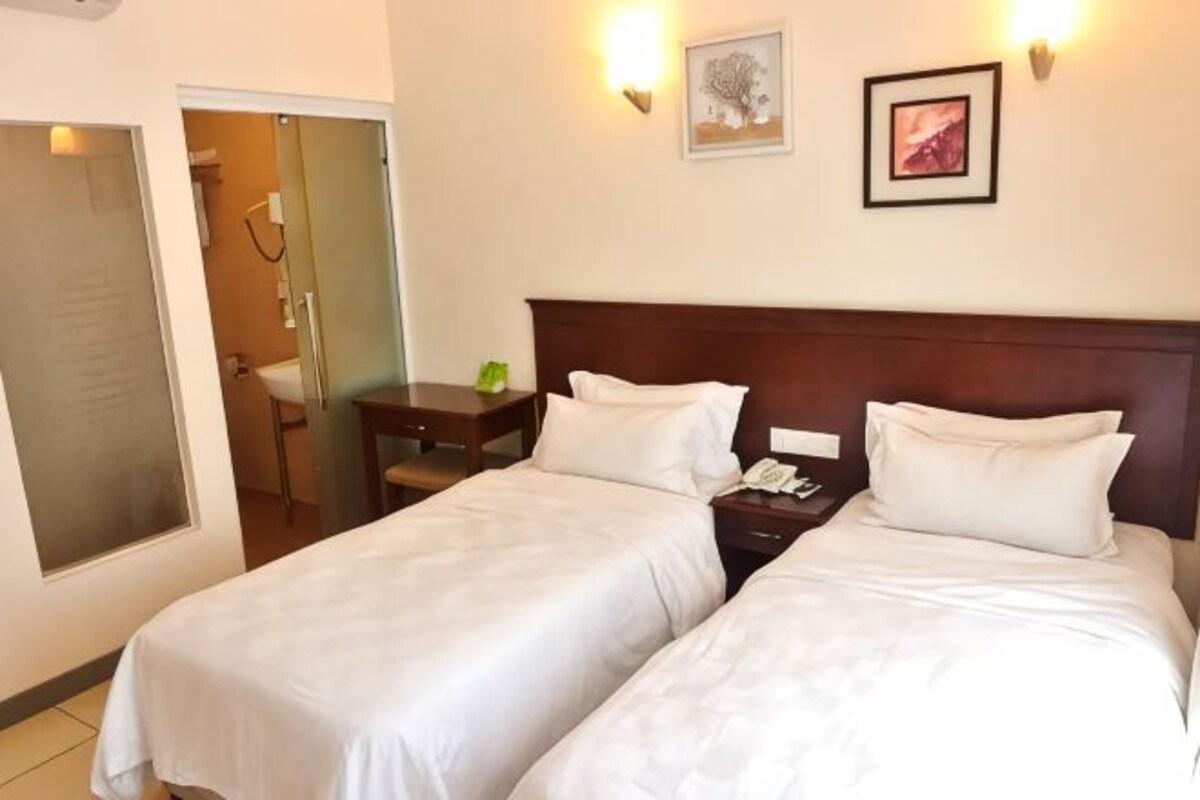 Een hotelkamer met twee bedden, een houten hoofdeinde, een nachtkastje met een lamp en een deur naar een badkamer.