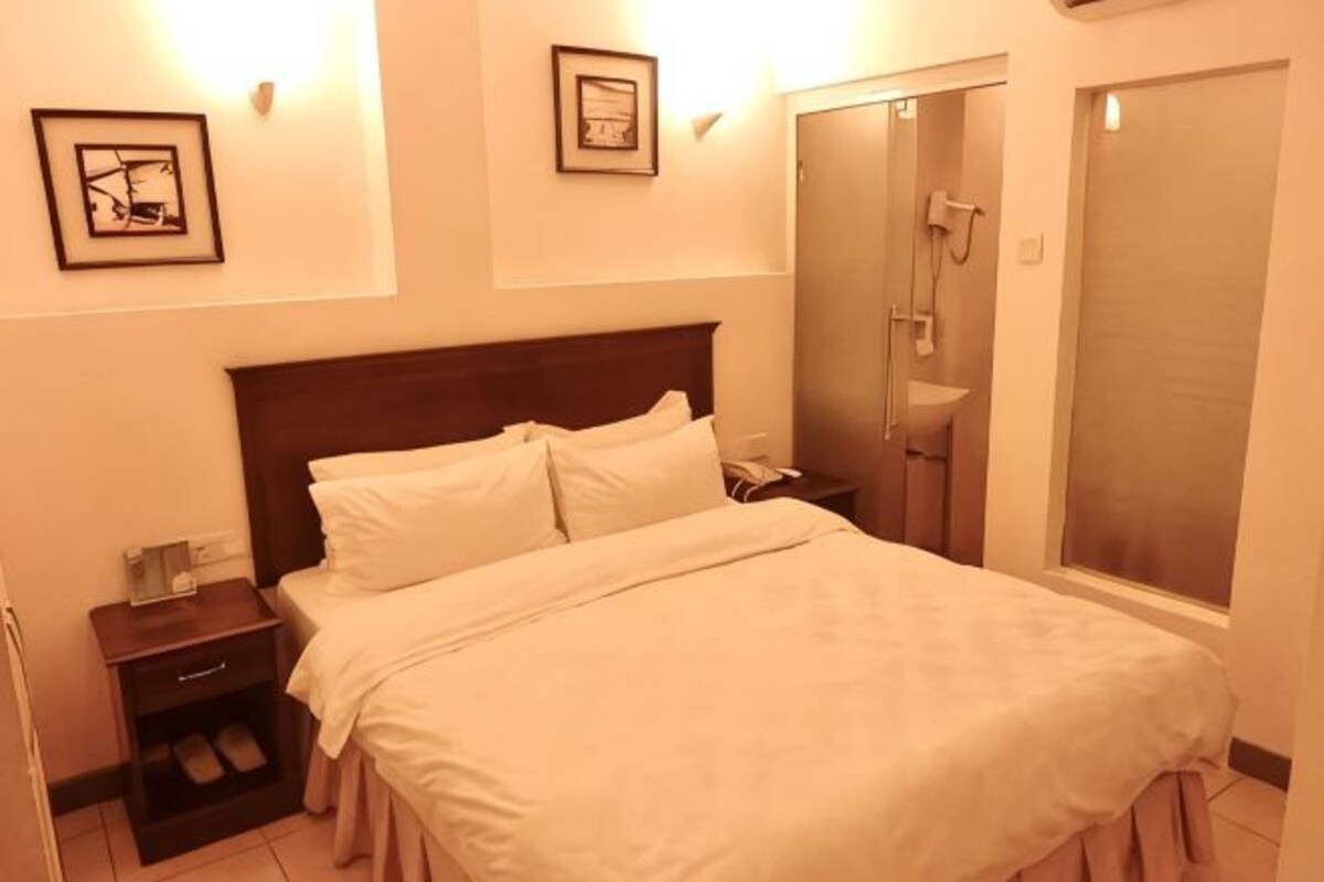 Een hotelkamer met een bed, nachtkastje en een douchehoek.