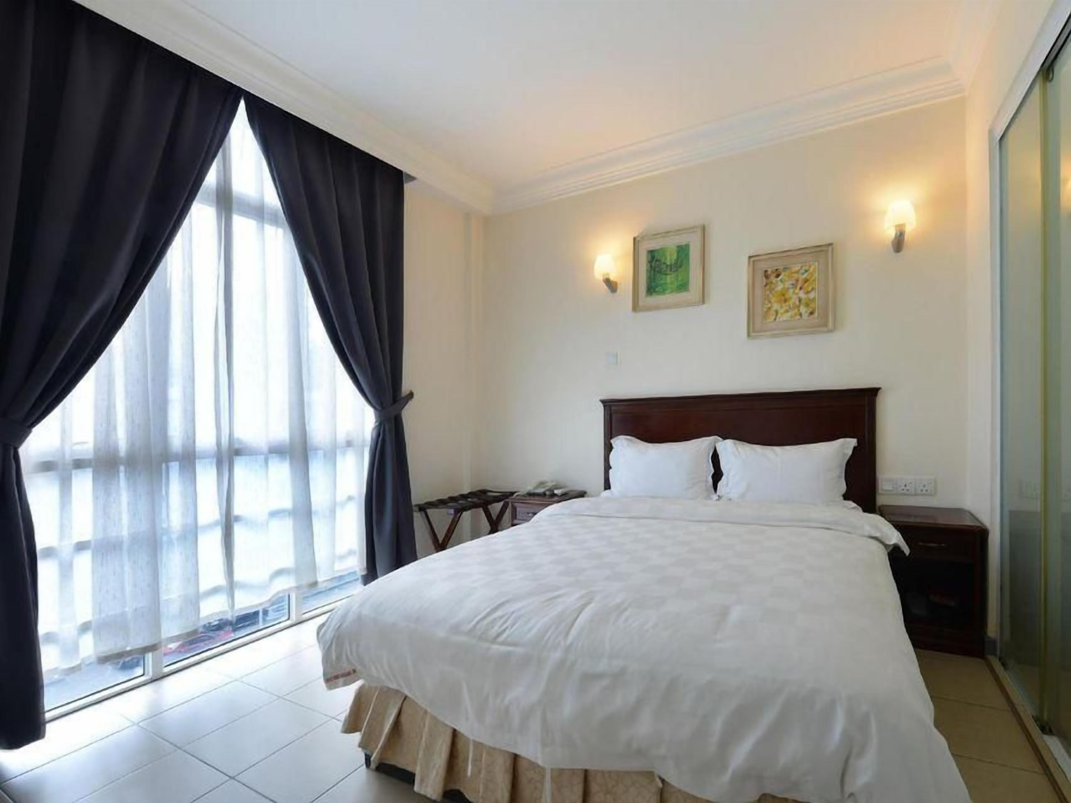 A hotel room with a large bed, a nightstand, a chair, and a window with curtains.