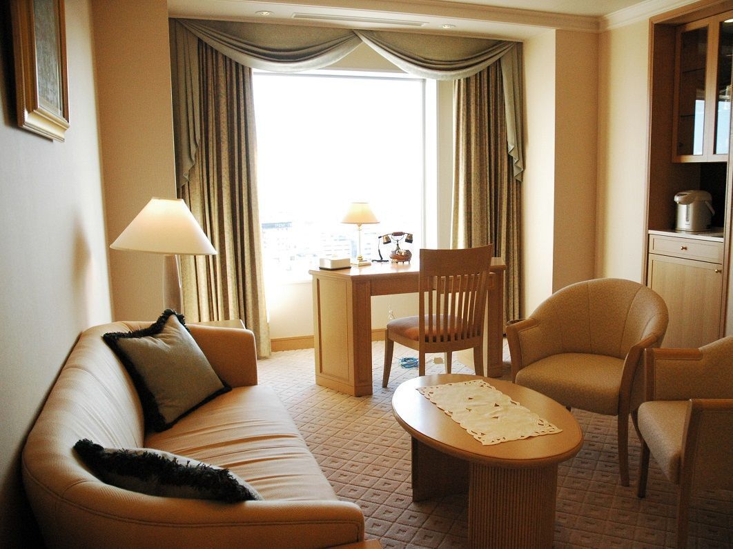 Ein Hotelzimmer mit einer Couch, einem Esstisch, einem Stuhl, einer Lampe und Blick auf die Stadt.