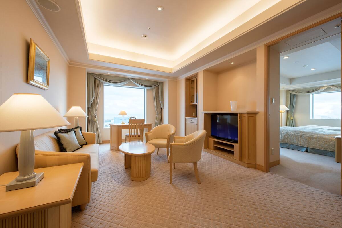 A hotel room with a sofa, chairs, a TV, a dining table, and a bed.