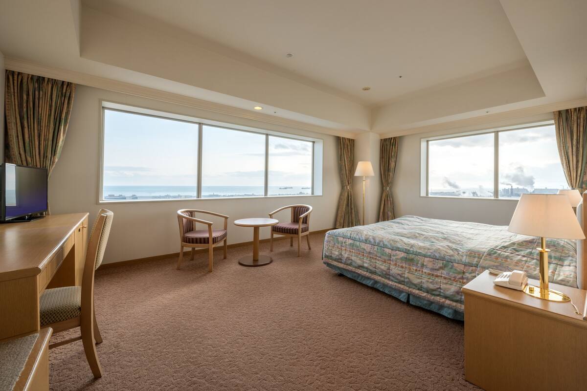 A hotel room with a large bed, a desk with a chair, a small table, and a TV.