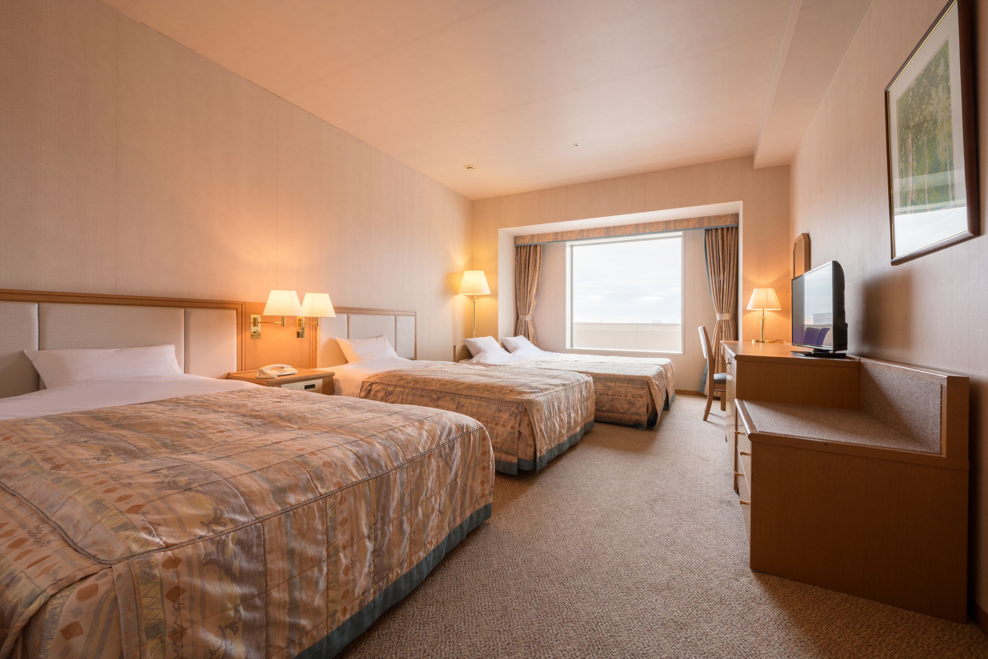 A hotel room with two beds, a desk, a chair, a TV, and a window with curtains.