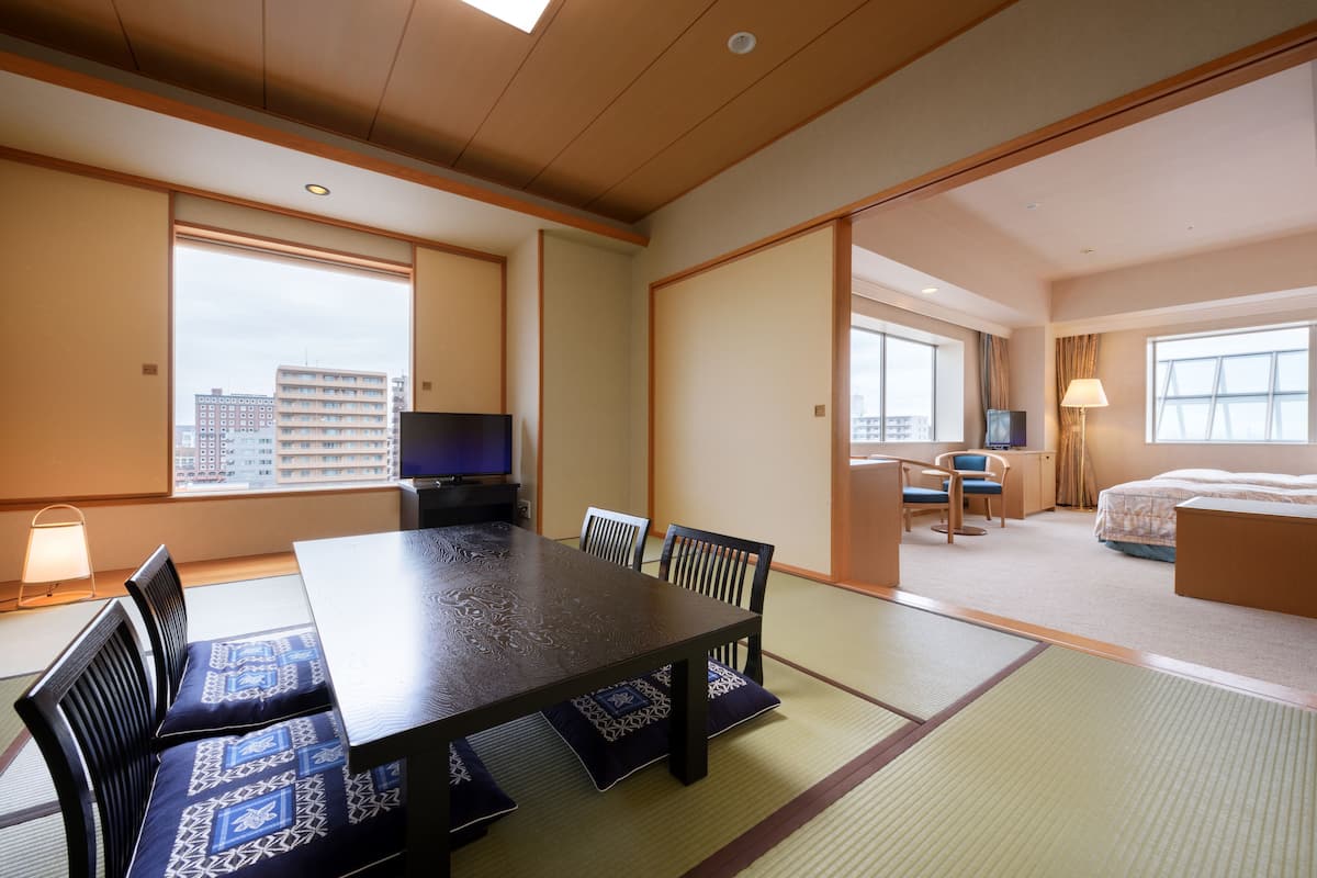 A hotel room with tatami flooring, a dining table with chairs, a bed, and a television.