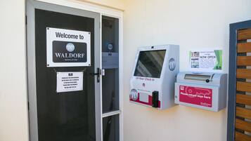 A hotel entrance with a welcome sign, a 24-hour check-in machine, and a key return box.