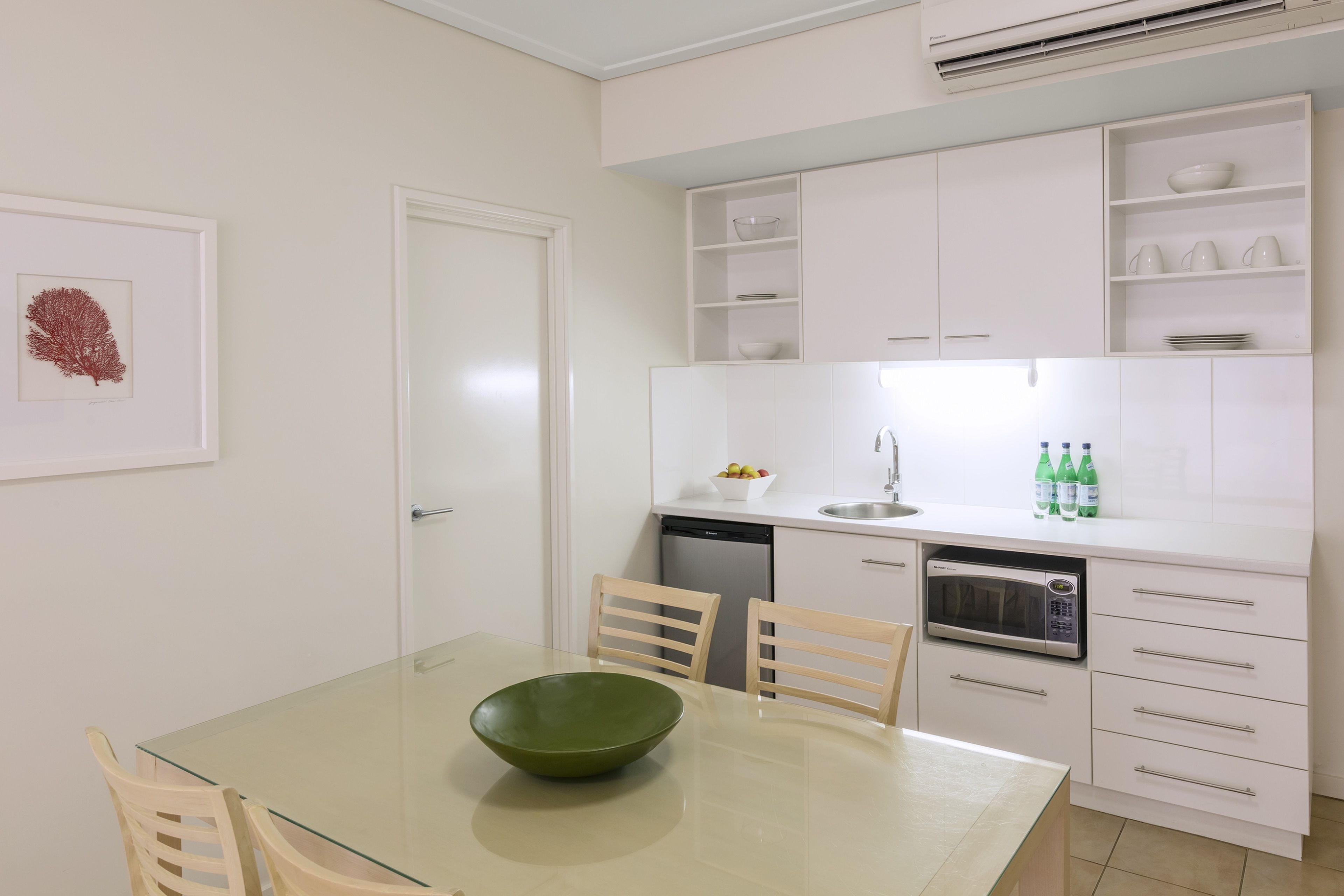 A modern kitchen with white cabinets, a glass dining table, and a green bowl.
