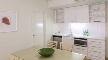 A modern kitchen with white cabinets, a glass dining table, and a green bowl.
