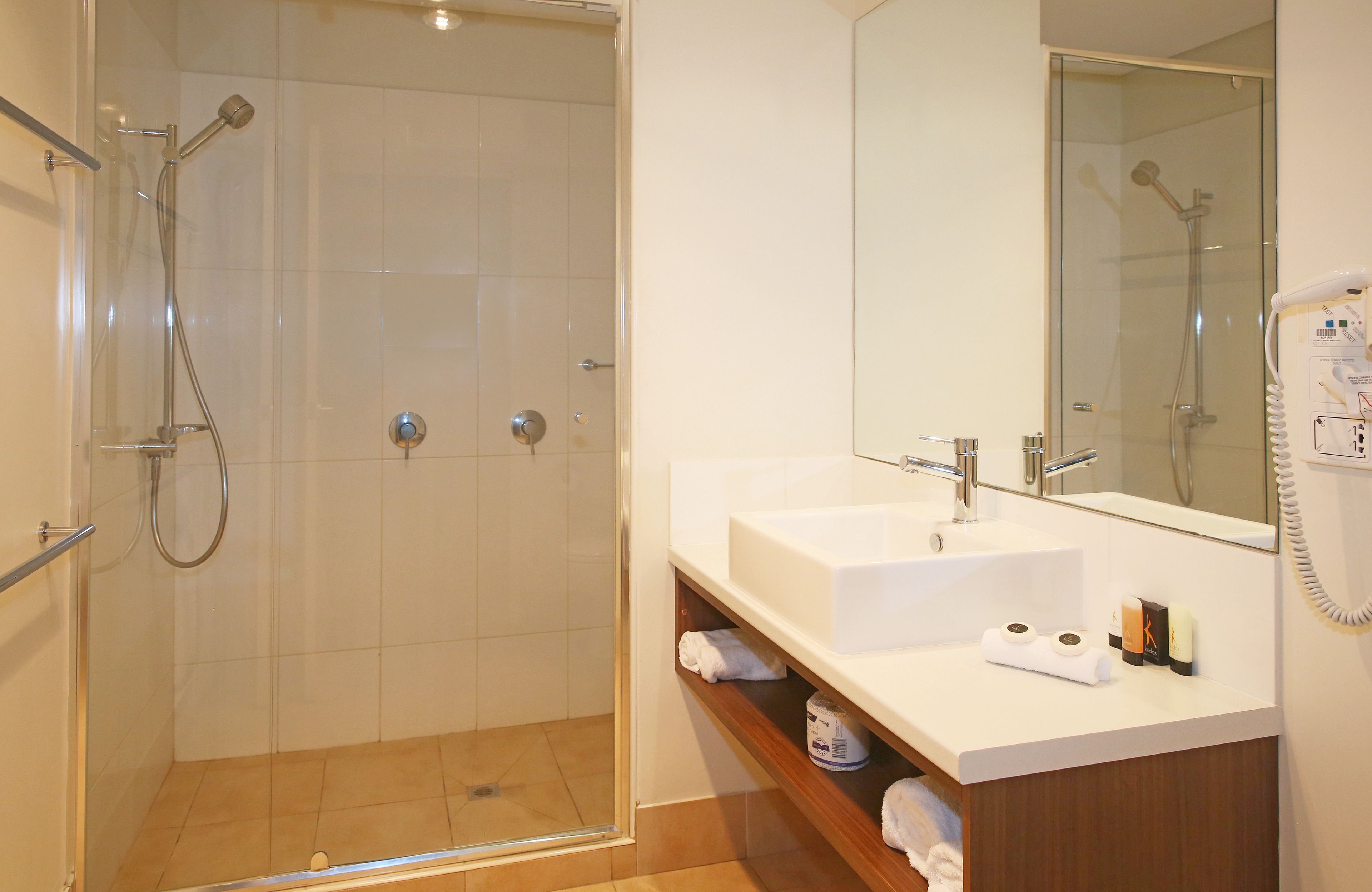 Un baño moderno con cabina de ducha de vidrio, un lavabo blanco y un espejo con teléfono.