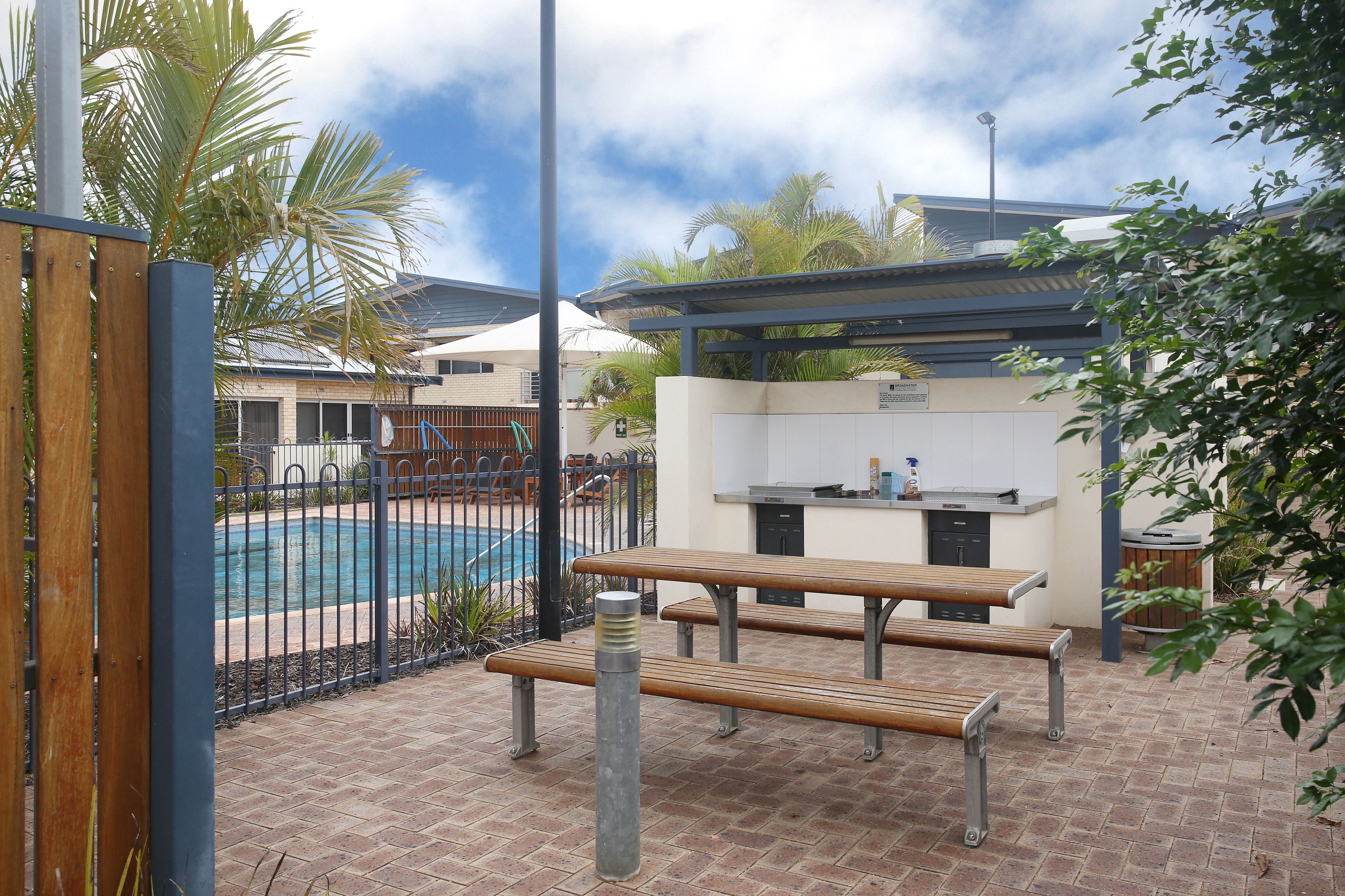 Un espace extérieur aménagé en terrasse, avec une piscine, des bancs en bois et un petit coin cuisine.