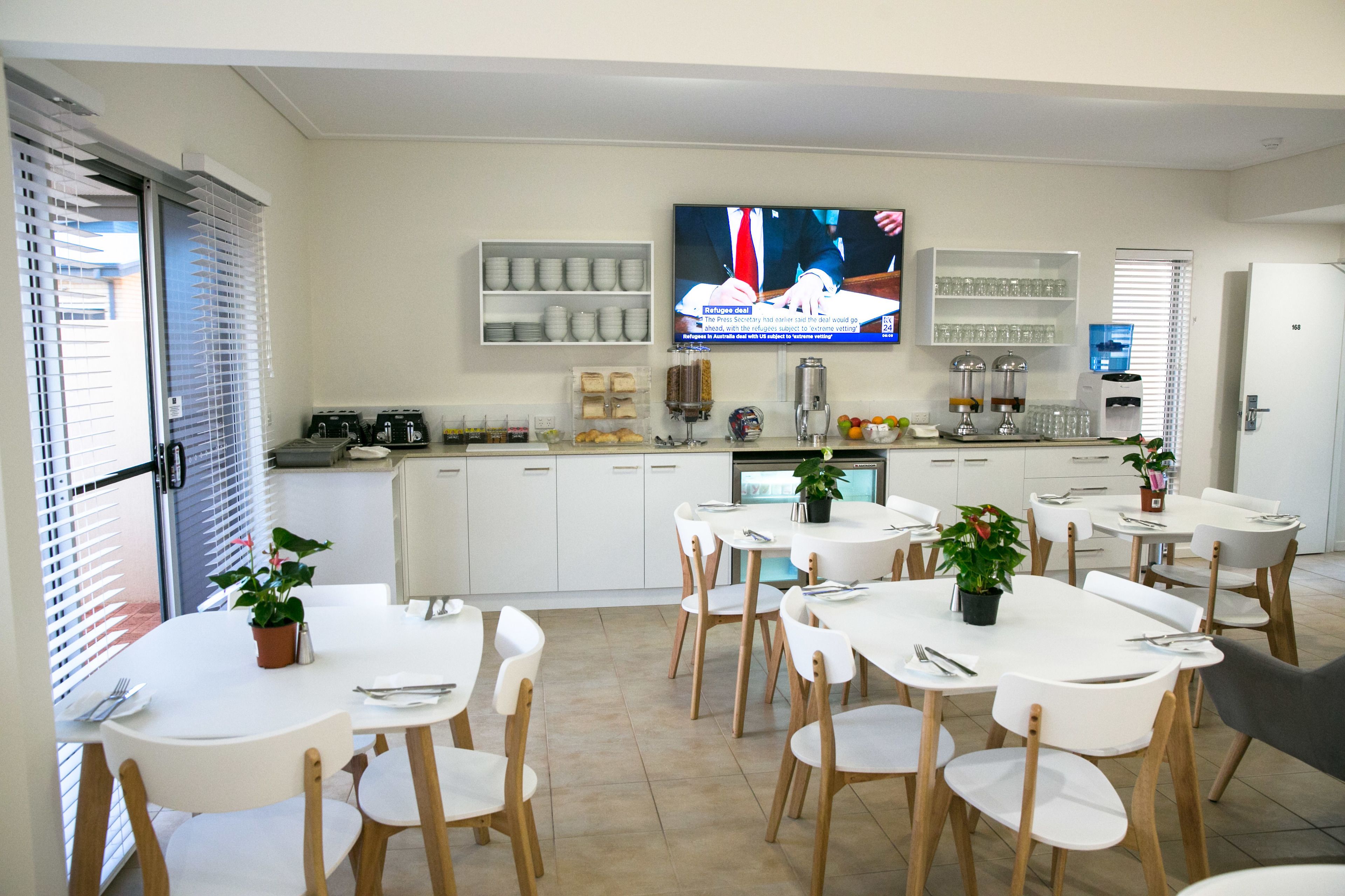 Une cuisine moderne avec des meubles blancs, un téléviseur à écran plat et un coin repas doté de tables et de chaises blanches.