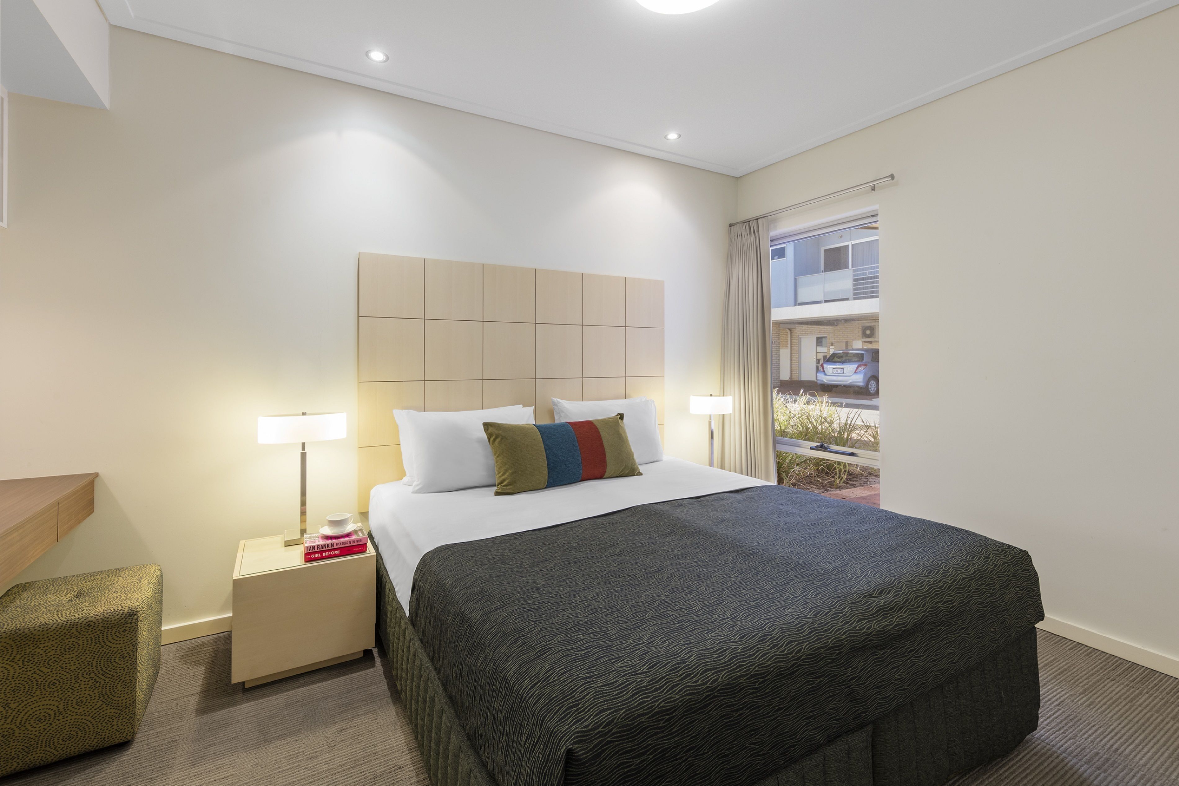 Une chambre d’hôtel avec un grand lit, une table de chevet avec une lampe, un petit coin salon et une vue sur l’extérieur.