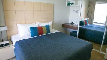 A hotel room with a large bed, a bedside table with a lamp, a small bedside table with a phone, a mirror, and a wardrobe.