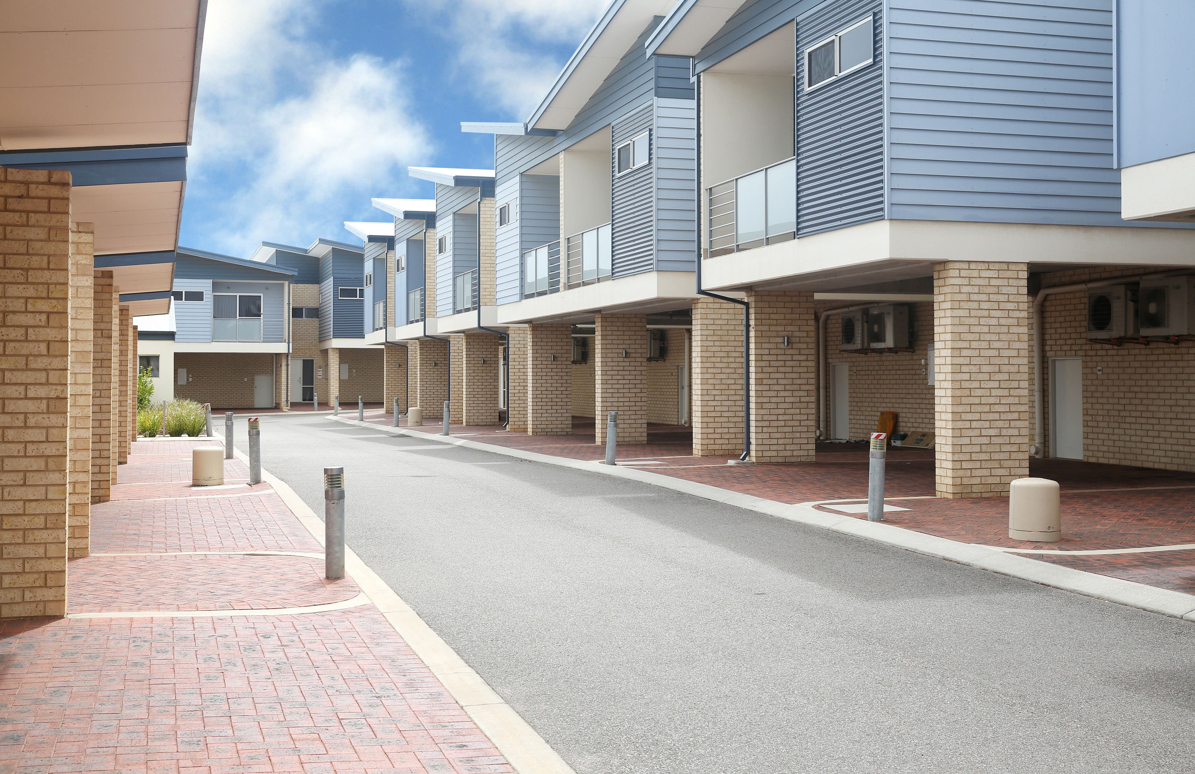 Una hilera de casas urbanas modernas con fachadas de ladrillo y balcones, un sendero pavimentado y bollards a lo largo de la calle.