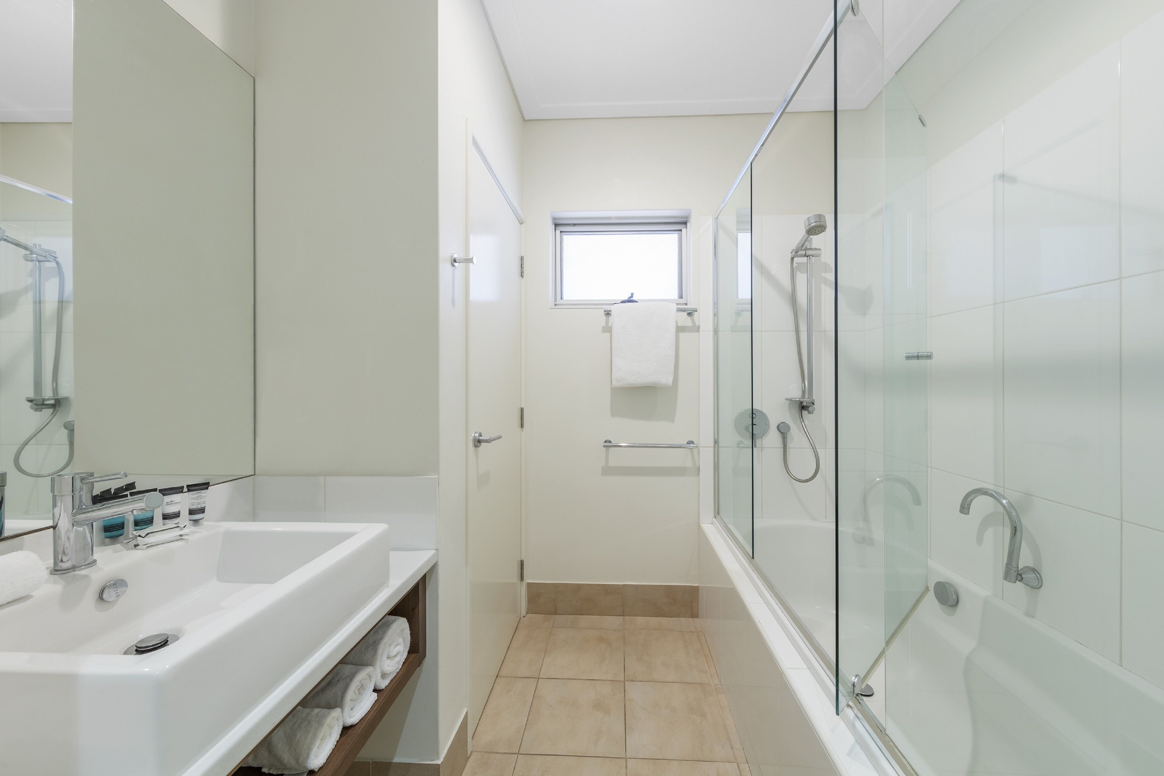 A modern bathroom with a glass-enclosed shower, a white sink with a vanity, and a small window above the door.