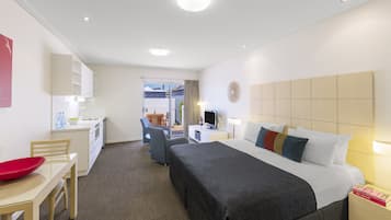 A hotel room with a bed, bedside table, desk, chair, and a small kitchenette.