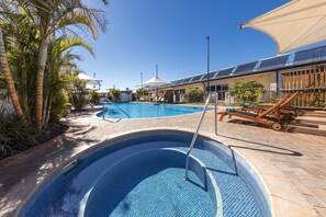 A swimming pool with a tiled edge, surrounded by palm trees and a building with solar panels. - Nesuto Geraldton (Beresford)