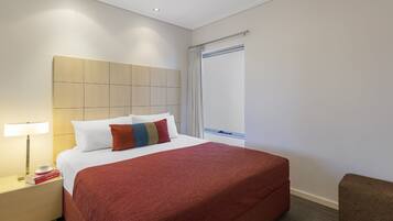 A hotel room with a large bed, a nightstand with a lamp, and a window with curtains.