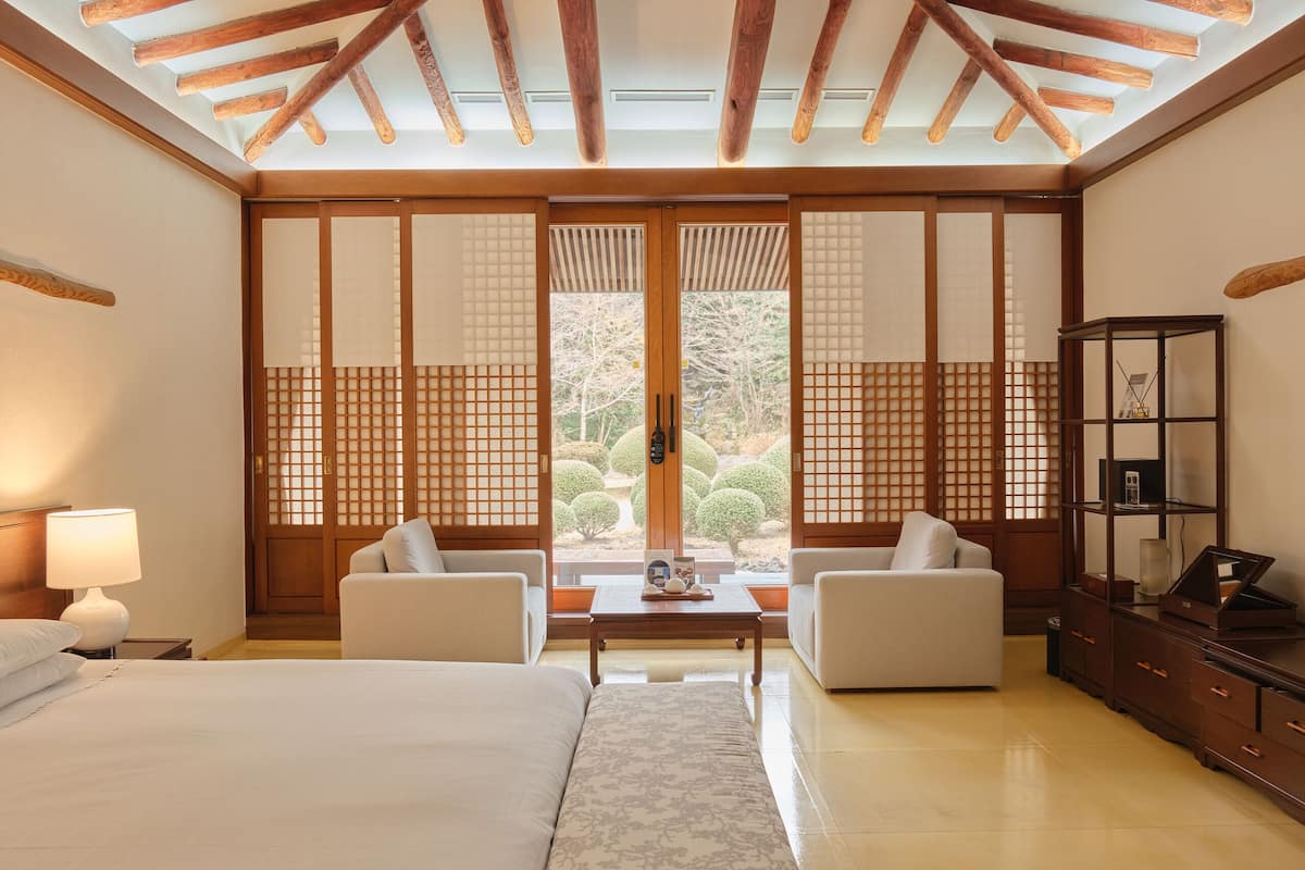 A hotel room with a bed, two white sofas, a small table with a teapot, and a wooden cabinet.
