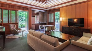 A modern living room with a wooden ceiling, a TV, sofas, a dining area, and large windows with blinds. - Podo Hotel (Seogwipo)